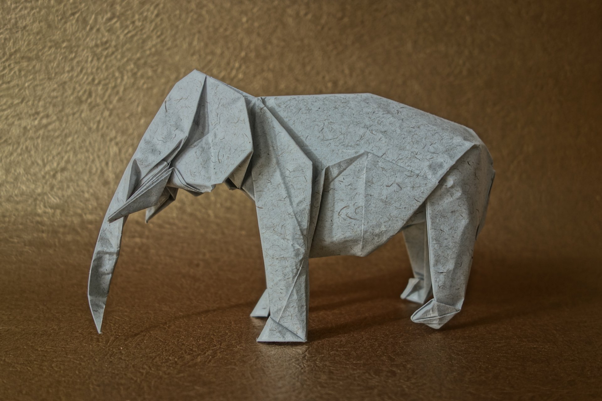Origami elephant, man-made paper sculpture on a textured gold surface, shown as a 5K Ultra HD PC desktop wallpaper and background.