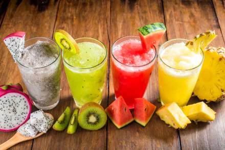 HD desktop wallpaper with a vibrant display of four colorful glasses filled with refreshing fruit juices: pitaya, kiwi, watermelon, and pineapple, accompanied by cut fruits on a wooden table background.
