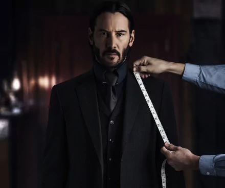 HD wallpaper featuring Keanu Reeves as John Wick from the movie John Wick: Chapter 2. He stands in a dark suit, while someone measures his shoulder with a tape measure.