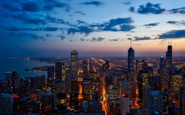 Aerial nighttime cityscape of Chicago with illuminated skyscrapers along Lake Michigan, showcasing the vibrant urban lights and skyline in this HD desktop wallpaper.