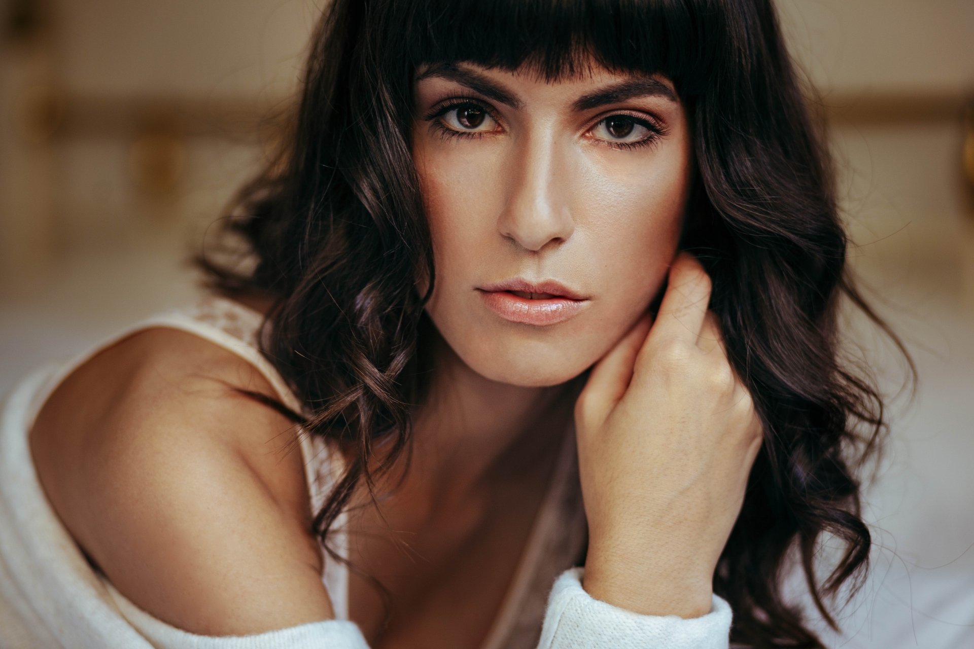 8K Ultra HD PC desktop wallpaper and background: close-up portrait of a brunette model woman with brown eyes, wavy hair, soft makeup, contemplative expression, hand near her face.