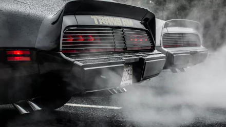 HD desktop wallpaper featuring the rear view of a classic Pontiac Trans Am vehicle emitting exhaust smoke in a moody, grayscale setting.