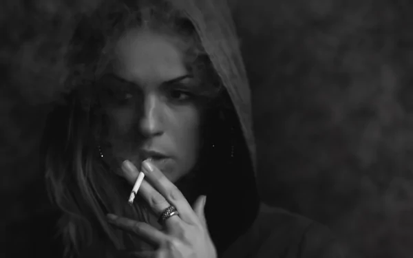 Black and white HD desktop wallpaper of a woman smoking, wearing a hooded jacket. The image captures a moody and contemplative atmosphere.