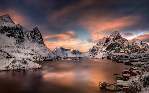 Stunning HD desktop wallpaper featuring a serene winter landscape in Lofoten, with snow-capped mountains and a calm body of water under a colorful, dramatic sky.