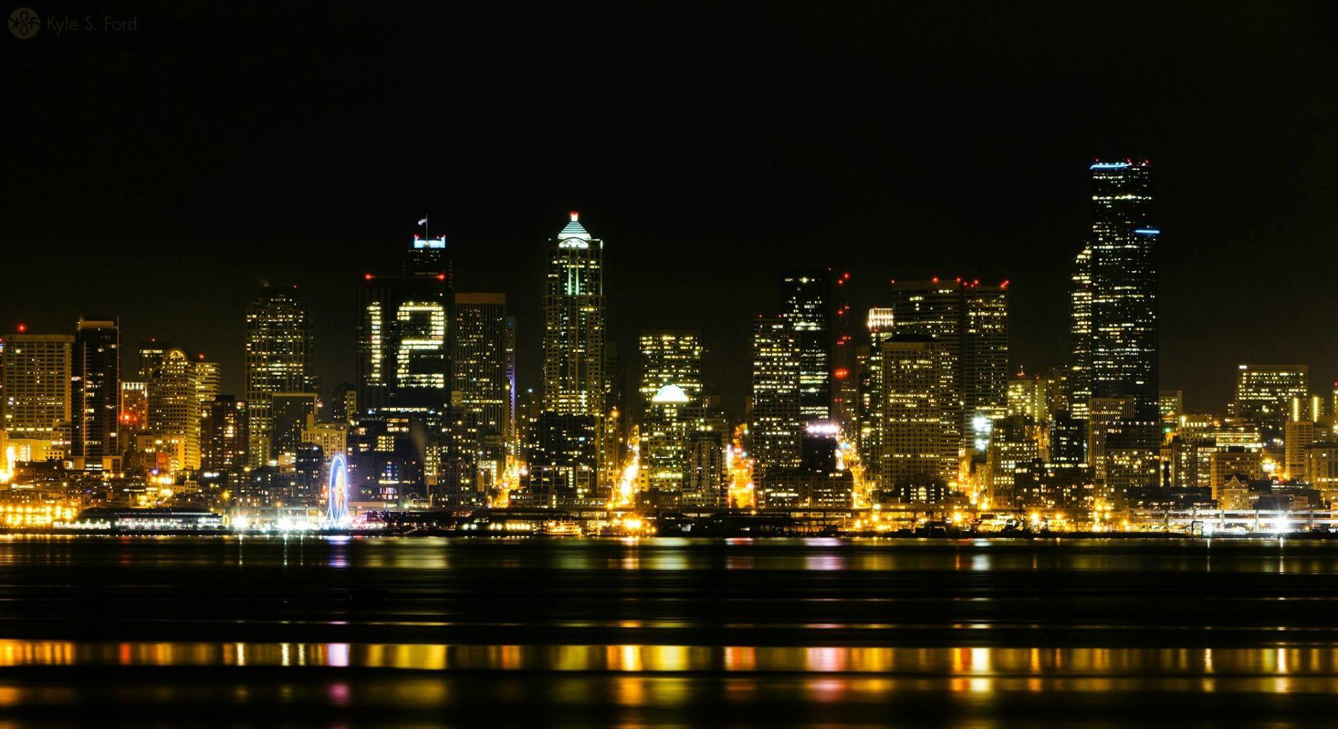 HD desktop wallpaper showcasing the Seattle skyline at night with illuminated buildings, including one displaying the number 12, reflecting over the water.