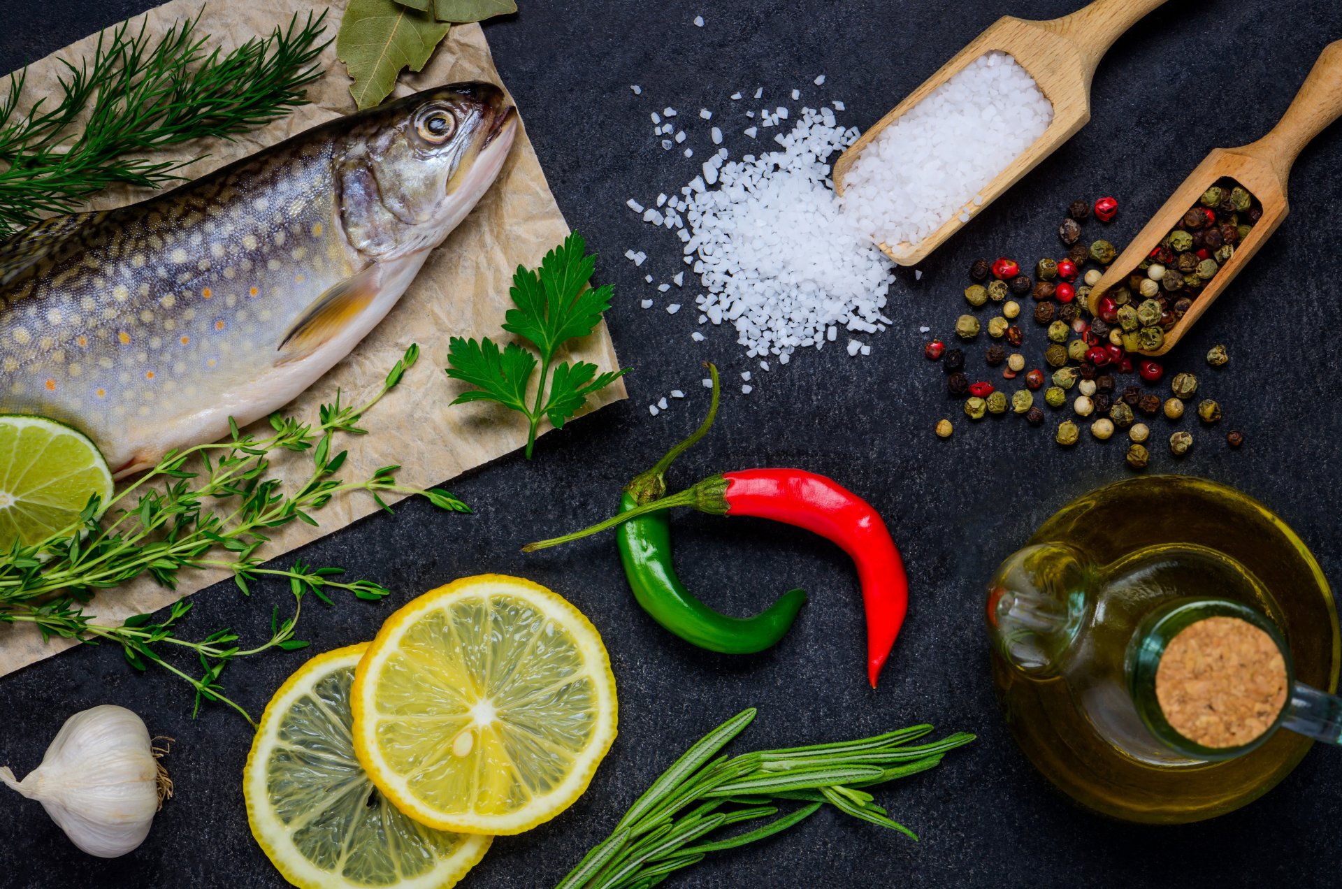 A 4K Ultra HD still life desktop wallpaper featuring fresh fish, lemon slices, chili peppers, herbs, coarse salt, peppercorns, and a bottle of oil arranged on a dark surface.