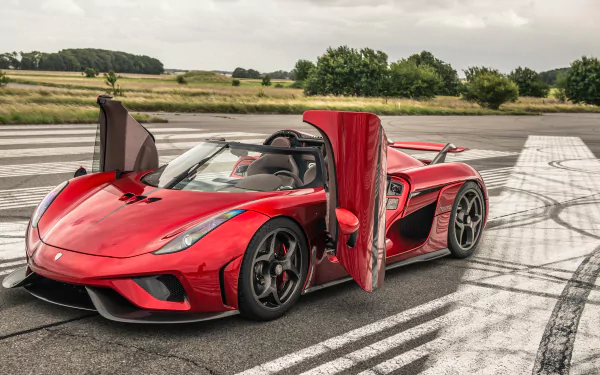 A stunning HD desktop wallpaper featuring a red Koenigsegg Regera supercar with its doors open, set against a scenic backdrop of an open road and green fields.