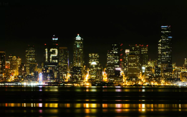 HD desktop wallpaper showcasing the Seattle skyline at night with illuminated buildings, including one displaying the number 12, reflecting over the water.