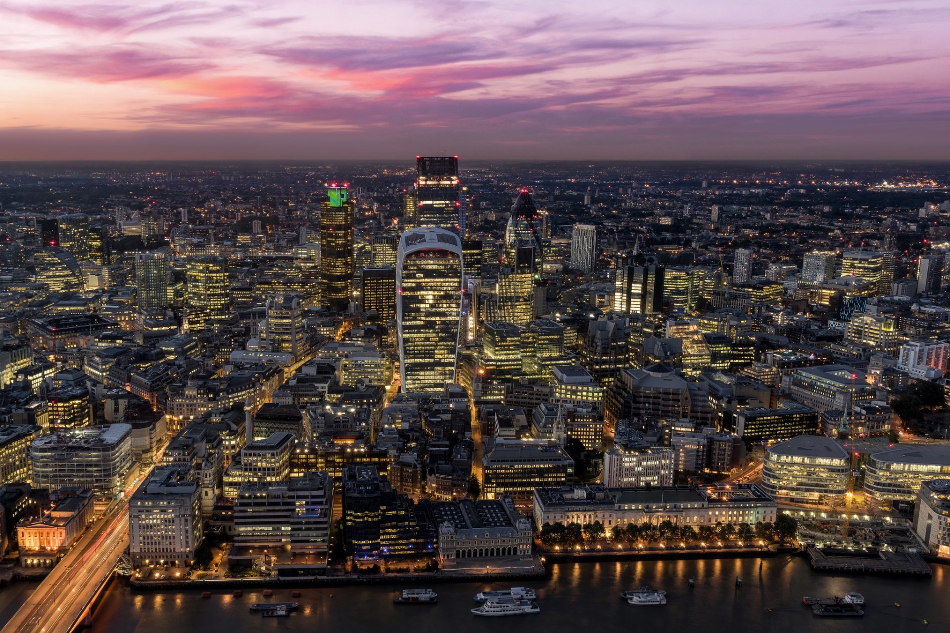Nighttime cityscape of London, showcasing illuminated skyscrapers and buildings along the river under a colorful dusk sky, captured in HD for a desktop wallpaper background.