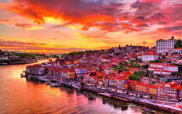 2K Quad HD desktop wallpaper of Porto, Portugal at sunset — colorful waterfront houses, boats along the river and the man-made historic cityscape under a fiery sky.