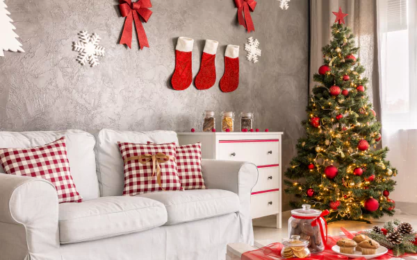 Cozy living room with a white sofa, plaid pillows, decorated Christmas tree, red stockings, and holiday ornaments creating a festive 4K Ultra HD desktop wallpaper.