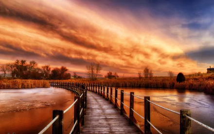 Boardwalk path curving over a frozen lake beneath a fiery sunset sky; man-made wooden walkway and reeds at dusk — 2K Quad HD PC desktop wallpaper/background.