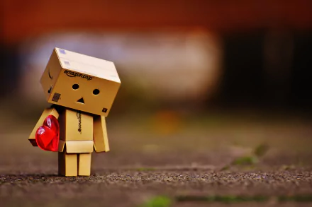 A small Danbo figure holding a red heart, standing on a textured surface with a blurred background, captured in 4K Ultra HD for a PC desktop wallpaper.