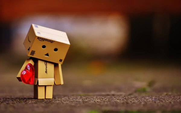 A small Danbo figure holding a red heart, standing on a textured surface with a blurred background, captured in 4K Ultra HD for a PC desktop wallpaper.