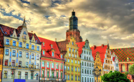 Vibrant, colorful historic buildings in Poland under dramatic clouds, captured in stunning 4K Ultra HD, showcasing intricate man-made architectural details.