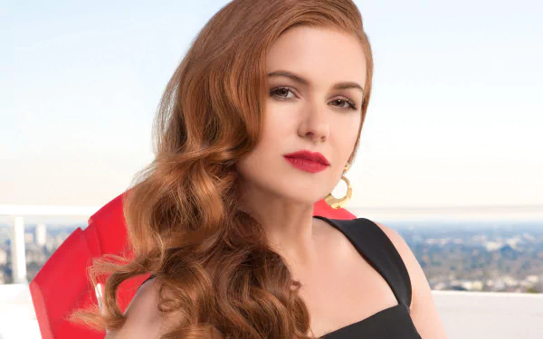 HD desktop wallpaper featuring Australian actress Isla Fisher with red lipstick, flowing red hair, and brown eyes against a blurred cityscape background.