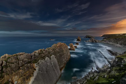 Sunset over the rugged coastline of Cantabria, Spain, with the calm sea meeting the horizon under a dramatic sky, captured in stunning HD for a desktop wallpaper.