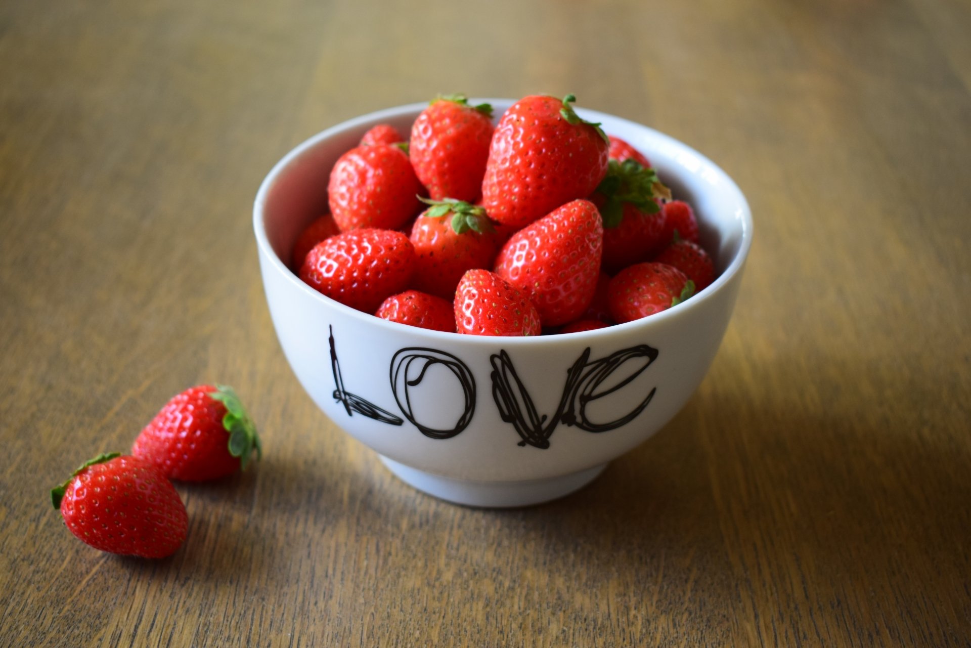A bowl filled with fresh strawberries on a wooden surface, with the word Love written on the bowl, captured in vibrant 4K Ultra HD quality.