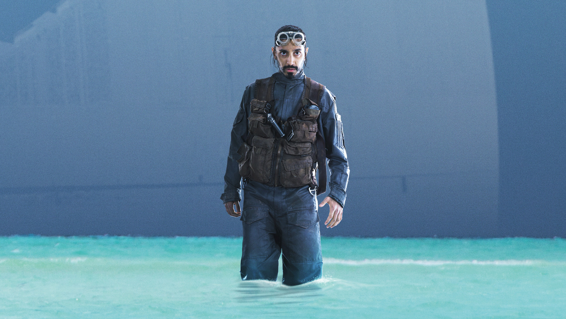 Bodhi Rook from the movie Rogue One: A Star Wars Story wading through shallow turquoise water, cinematic HD PC desktop wallpaper background.