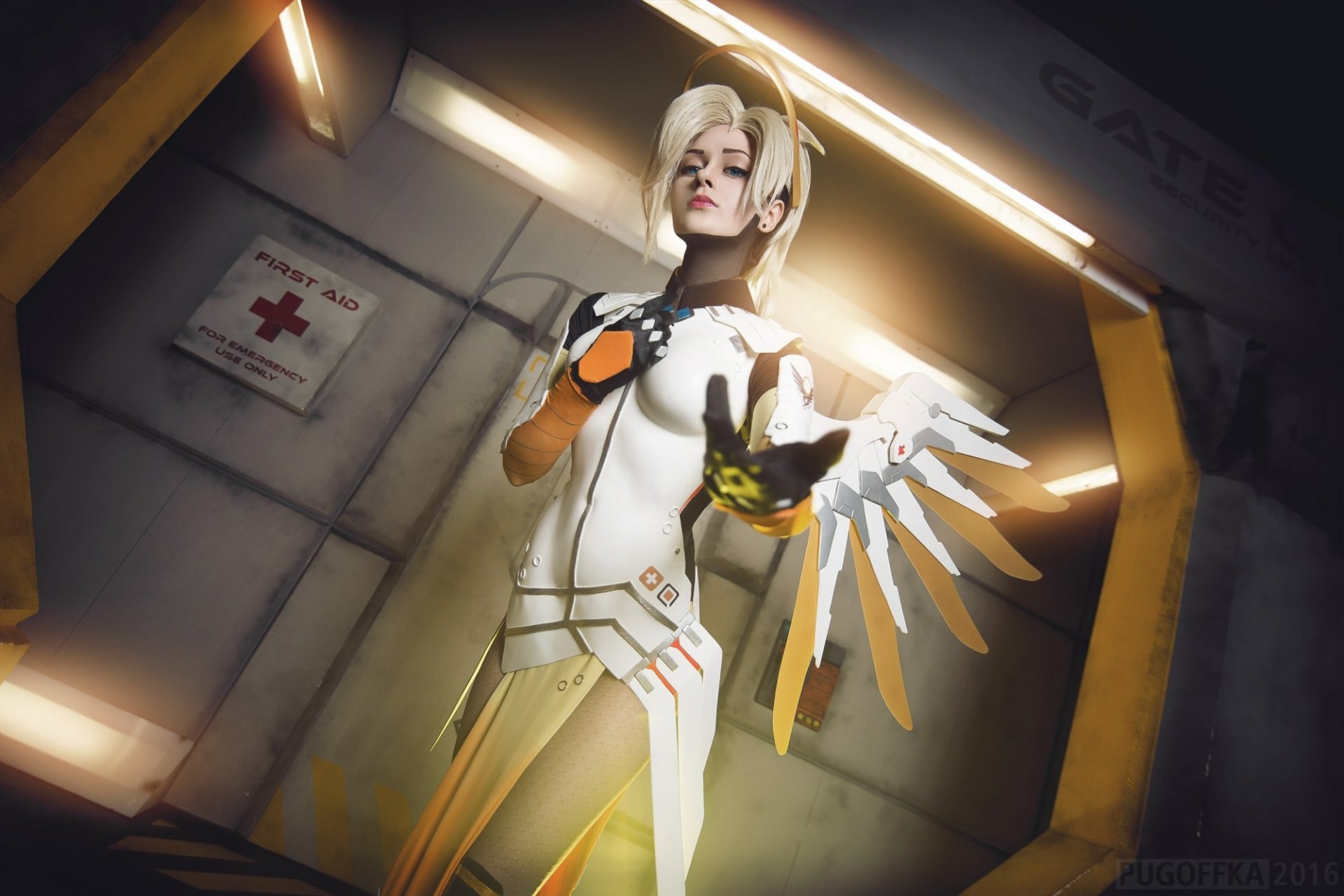 HD desktop wallpaper featuring a woman cosplaying as Mercy from Overwatch, standing determinedly with illuminated wings in a futuristic setting.