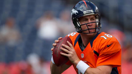 HD wallpaper of a focused Peyton Manning in an orange jersey, preparing to throw a football on the field.