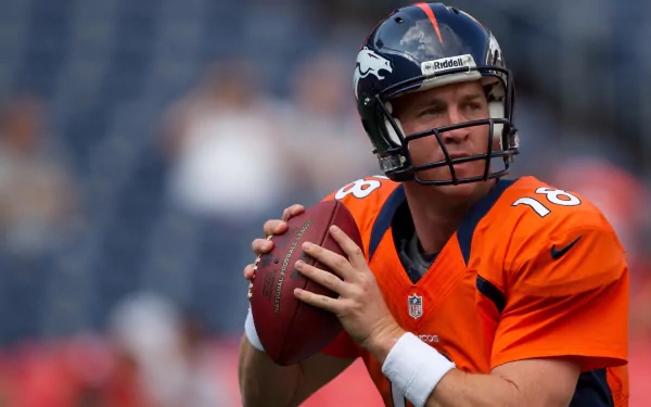 HD wallpaper of a focused Peyton Manning in an orange jersey, preparing to throw a football on the field.