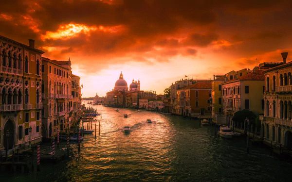 Sunset over the Grand Canal in Venice, Italy, with boats gliding through the water and historic buildings lining the cityscape under dramatic clouds.