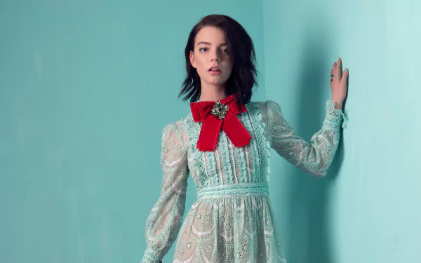 Anya Taylor-Joy, American actress and model with brown eyes and brunette hair, poses in a detailed dress with a red bow against a light blue background.