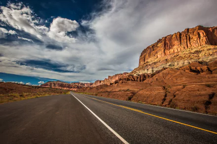 HD PC desktop wallpaper: a man-made highway through the Utah, USA desert with red rock cliffs and a dramatic cloud-filled sky.