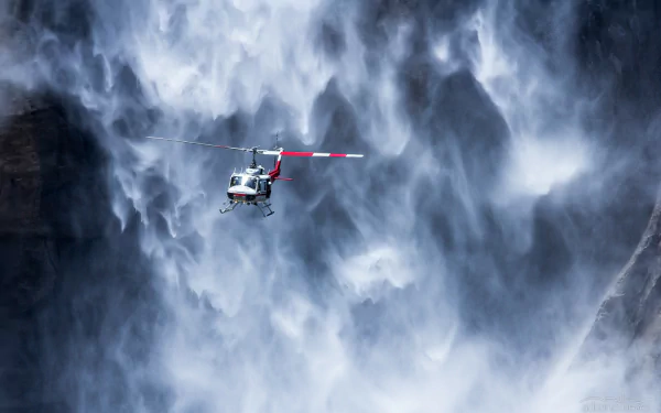 A Bell UH-1 Iroquois helicopter flies in front of a cascading waterfall, captured in this HD desktop wallpaper and background image.