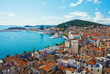 5K Ultra HD desktop wallpaper of a Croatian coastal city: terracotta-roofed houses, man-made harbor and marina on the blue sea and ocean with hills behind the town.