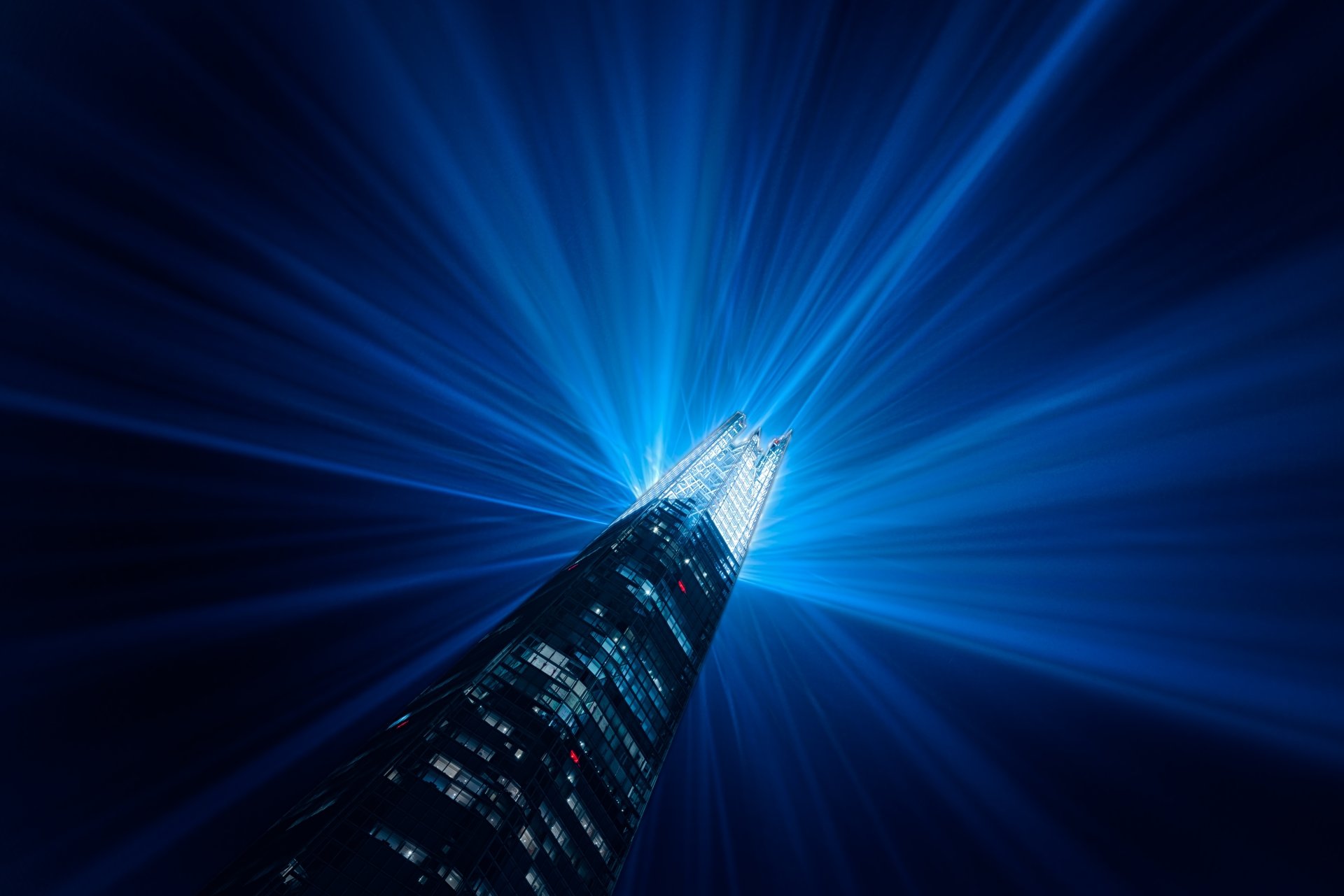 Blue-lit London skyscraper in 5K Ultra HD desktop wallpaper, man-made tower piercing night sky with radiating light beams.
