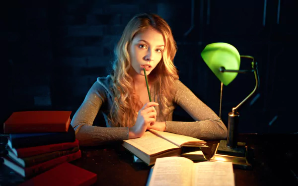 Blonde woman with hazel eyes, Alice Tarasenko, sits at a desk reading a book under a green lamp in this HD PC desktop wallpaper and background.