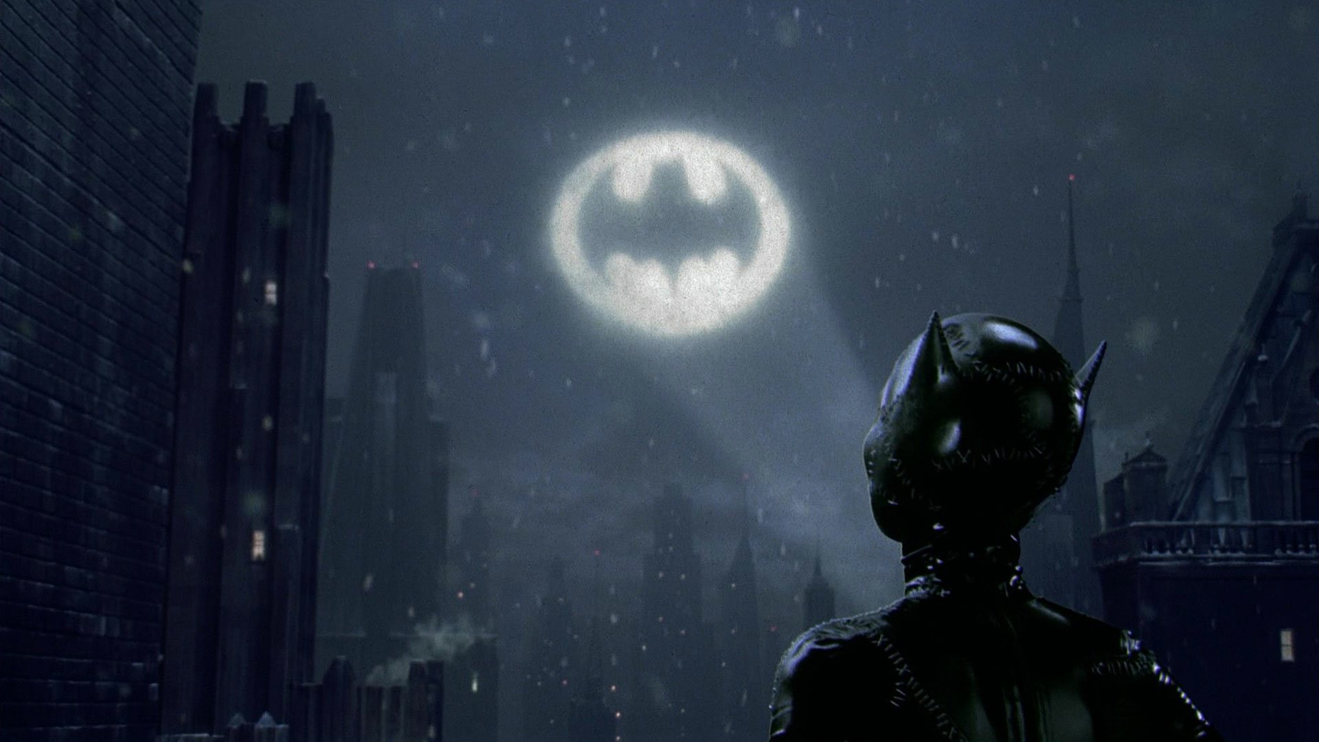 HD PC desktop wallpaper and background from the Batman Returns movie: silhouetted Catwoman watches the glowing Bat-Signal over a snowy Gotham skyline at night.