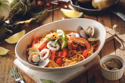 HD desktop wallpaper of a seafood meal featuring shrimp, clams, mussels, and pasta, garnished with herbs and lemon wedges on a rustic wooden table.