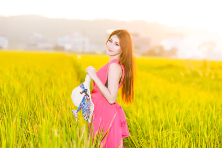 Asian woman with brunette hair wearing a pink dress and holding a hat stands in a sunlit field, captured with depth of field in vibrant 4K Ultra HD resolution.