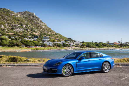 Blue Porsche Panamera car parked beside a coastal inlet with hillside homes; a 4K Ultra HD PC desktop wallpaper background showcasing the Porsche vehicle.