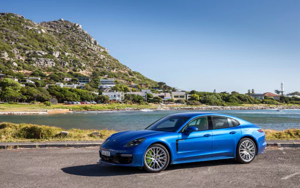 Blue Porsche Panamera car parked beside a coastal inlet with hillside homes; a 4K Ultra HD PC desktop wallpaper background showcasing the Porsche vehicle.