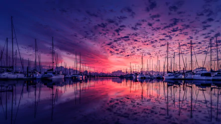 HD desktop wallpaper showing a stunning sunset over a harbor, with boats reflected in the calm water, and vibrant clouds filling the sky.