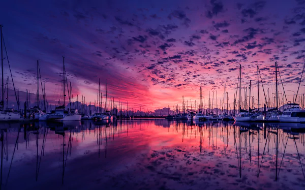 HD desktop wallpaper showing a stunning sunset over a harbor, with boats reflected in the calm water, and vibrant clouds filling the sky.