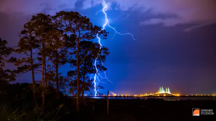 HD PC desktop wallpaper showing striking lightning illuminating a blue sky above silhouetted trees and a distant illuminated bridge over the earth at night.
