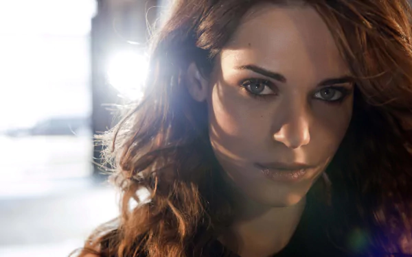HD PC desktop wallpaper featuring a close-up of a woman from the TV show Nikita, with intense eyes and flowing hair illuminated by bright backlighting.