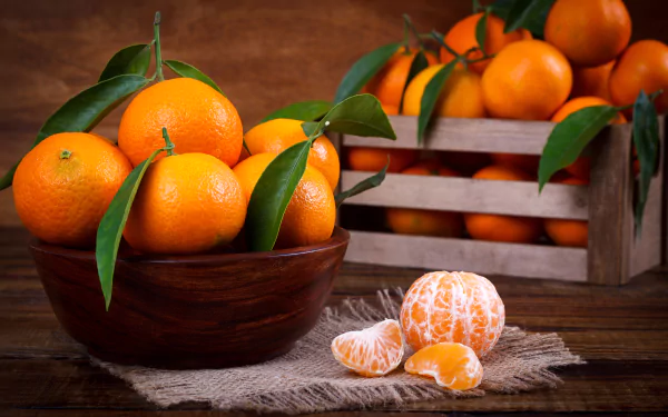 A vibrant still life of fresh mandarins in a wooden bowl and crate, set against a rustic wooden background in 4K Ultra HD quality.