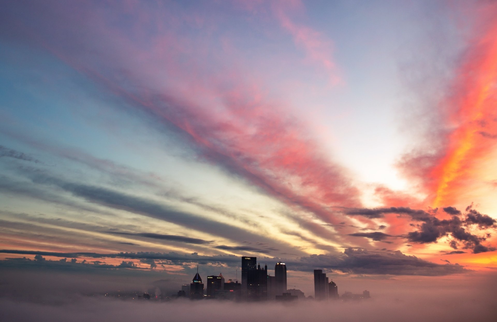 Pittsburgh skyscrapers rising through thick fog under streaked clouds and colorful sky — HD PC desktop wallpaper of a USA city skyline.