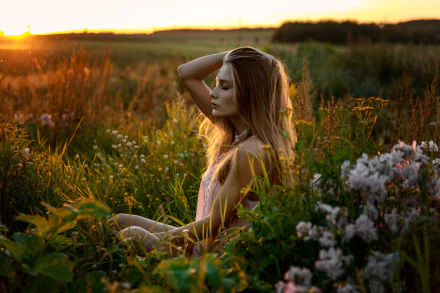 Blonde woman model sits peacefully in a sunlit field at sunrise, surrounded by wildflowers, captured with shallow depth of field in this HD desktop wallpaper.