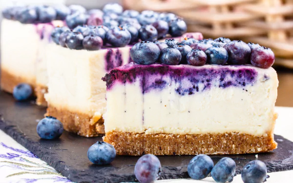 HD desktop wallpaper featuring slices of blueberry cheesecake with a graham crust, topped with fresh blueberries and blueberry sauce, showcasing a delicious dessert pastry.