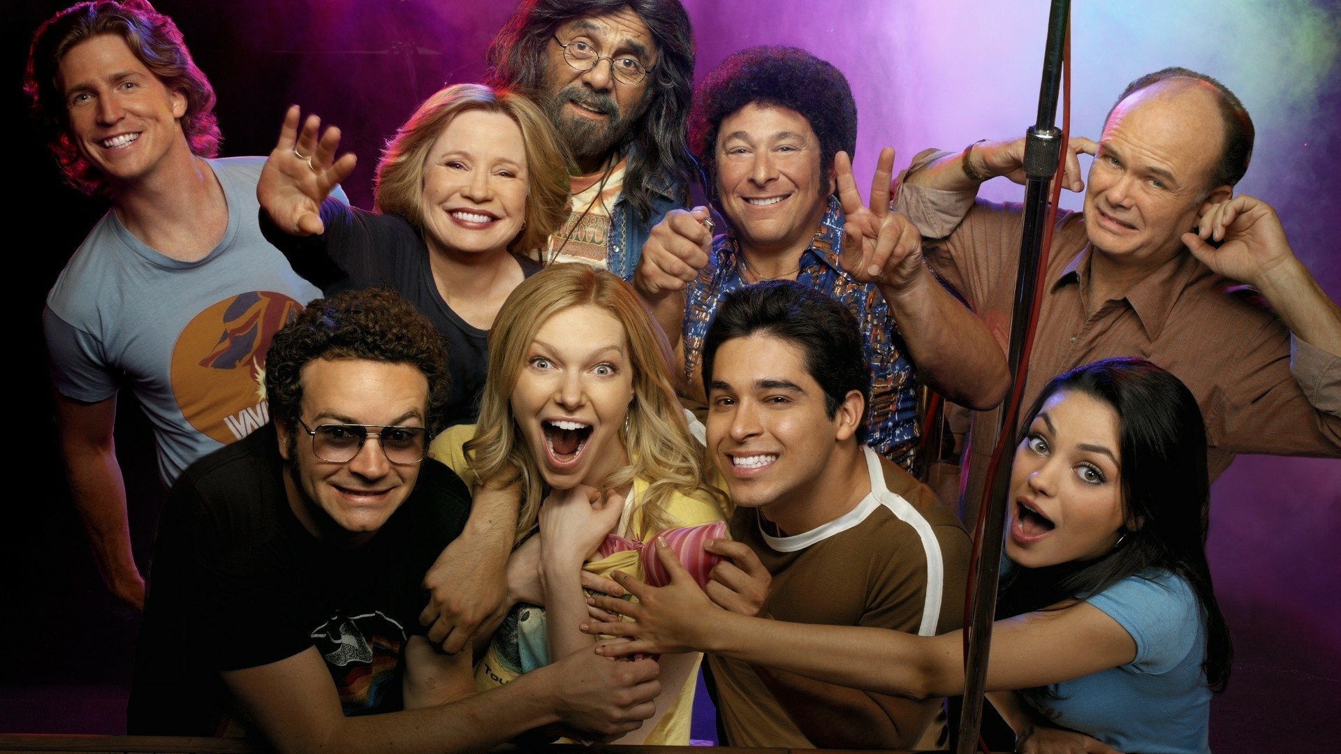 HD PC desktop wallpaper: colorful group portrait of characters from the TV show That '70s Show, smiling and posing against a purple-lit backdrop.