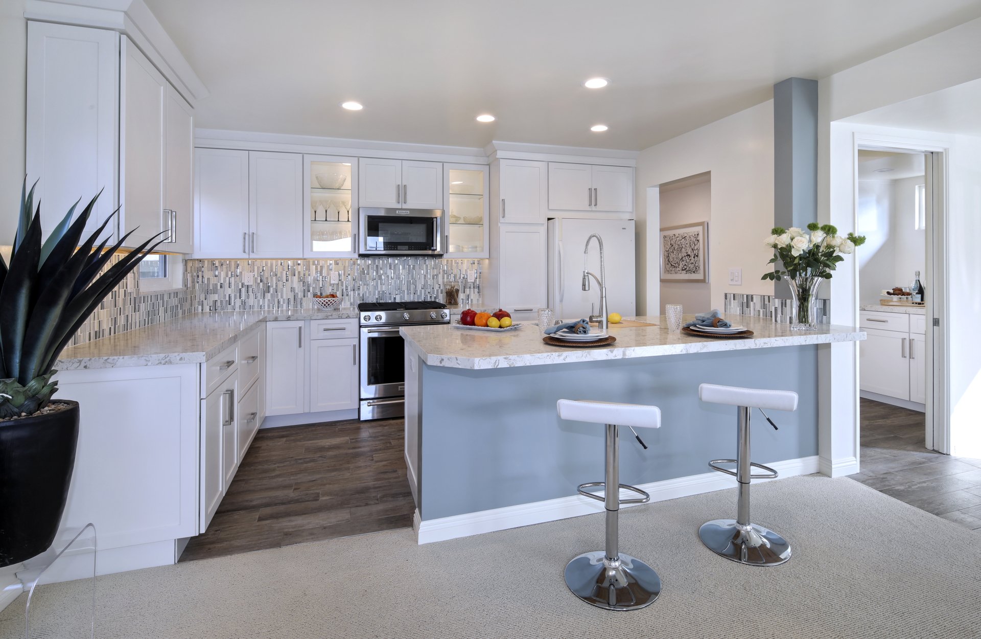 Modern kitchen room featuring sleek man-made furniture with white cabinets, a central island with bar stools, and stainless steel appliances. 4K Ultra HD PC wallpaper.