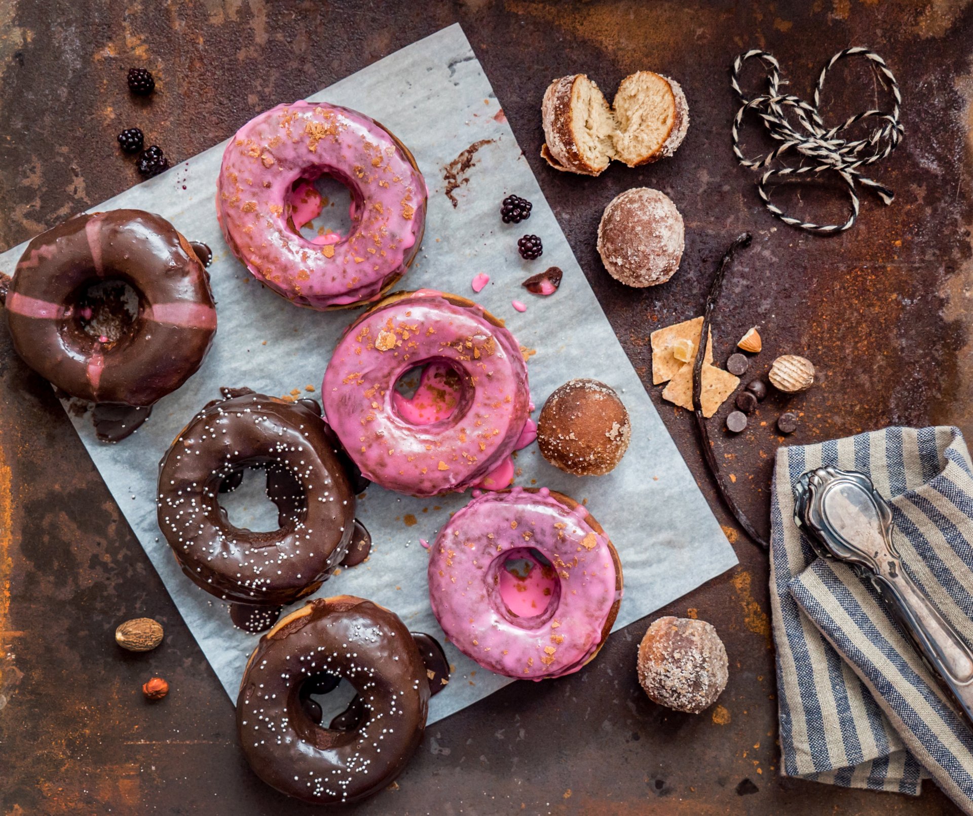 2K Quad HD PC desktop wallpaper and background: still life of assorted pink and chocolate-glazed doughnuts, truffles and berries on parchment and a rustic backdrop.