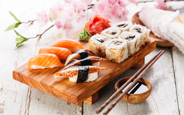 HD desktop wallpaper featuring a still life of assorted sushi, including rice, fish, and seafood, artfully arranged on a wooden board with chopsticks and cherry blossoms.
